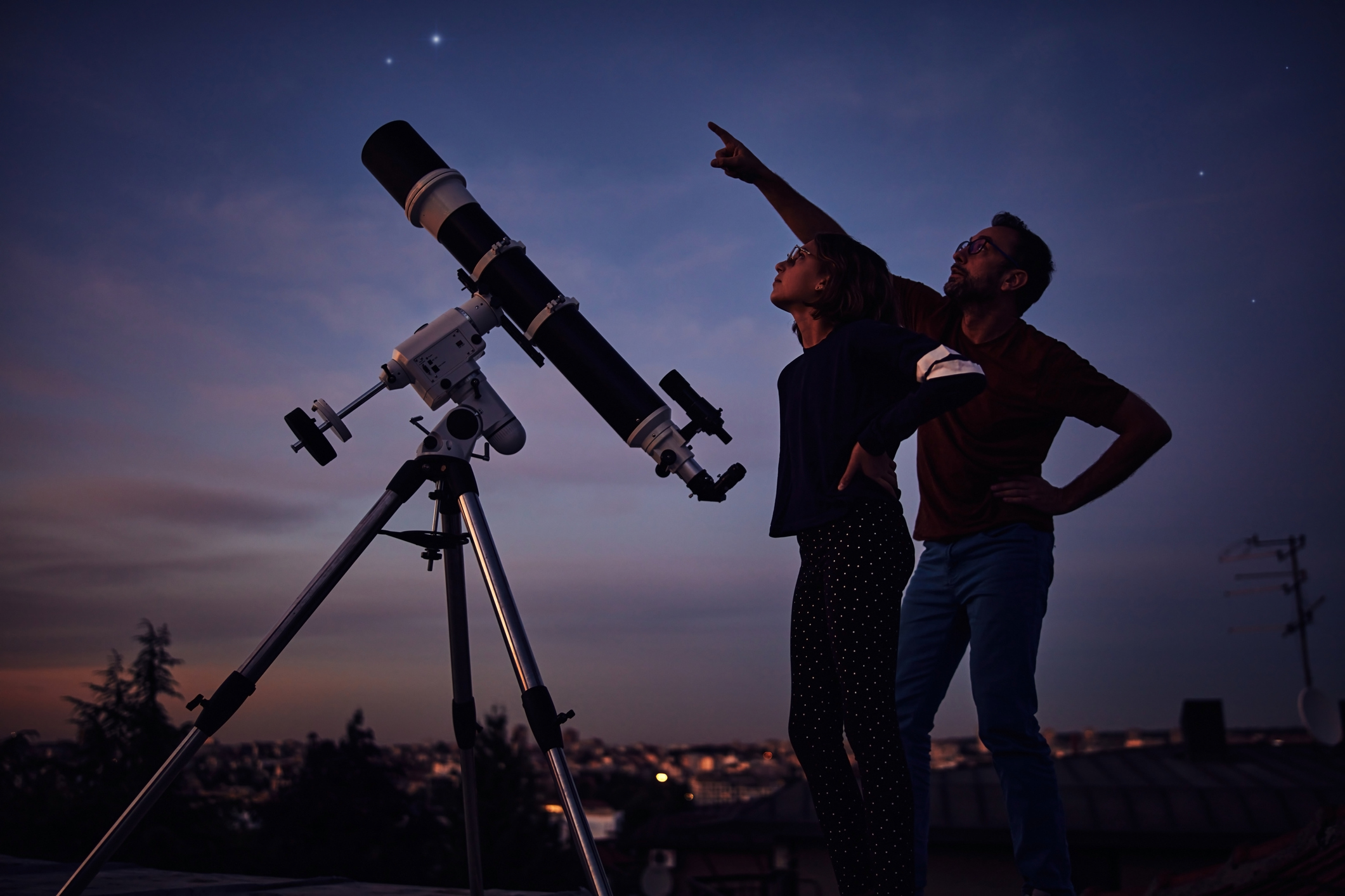 Muž a žena pozorují noční oblohu hvězdářským dalekohledem 