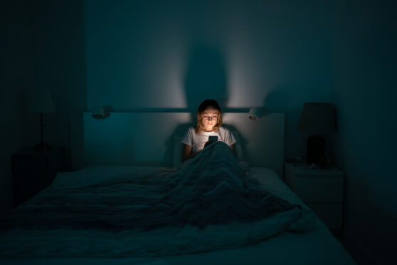 Žena sedí na posteli s mobilem