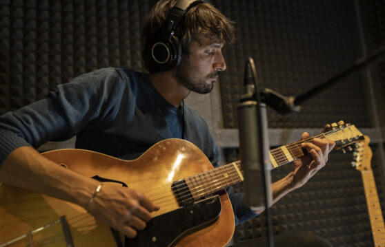 Muž hraje na kytaru v nahrávacím studiu