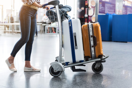Žena veze kufry na vozíku na letišti