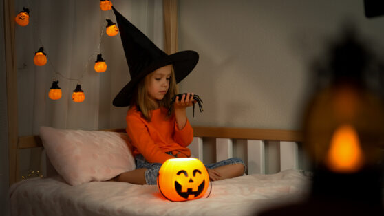 Dívka v čarodějnickém klobouku si hraje s pavoukem v posteli
