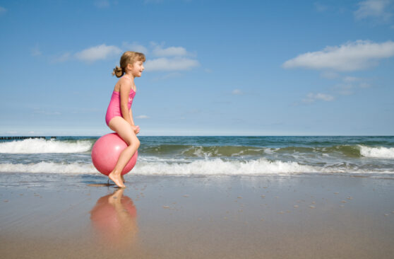 Holčička skáče na míči na pláži